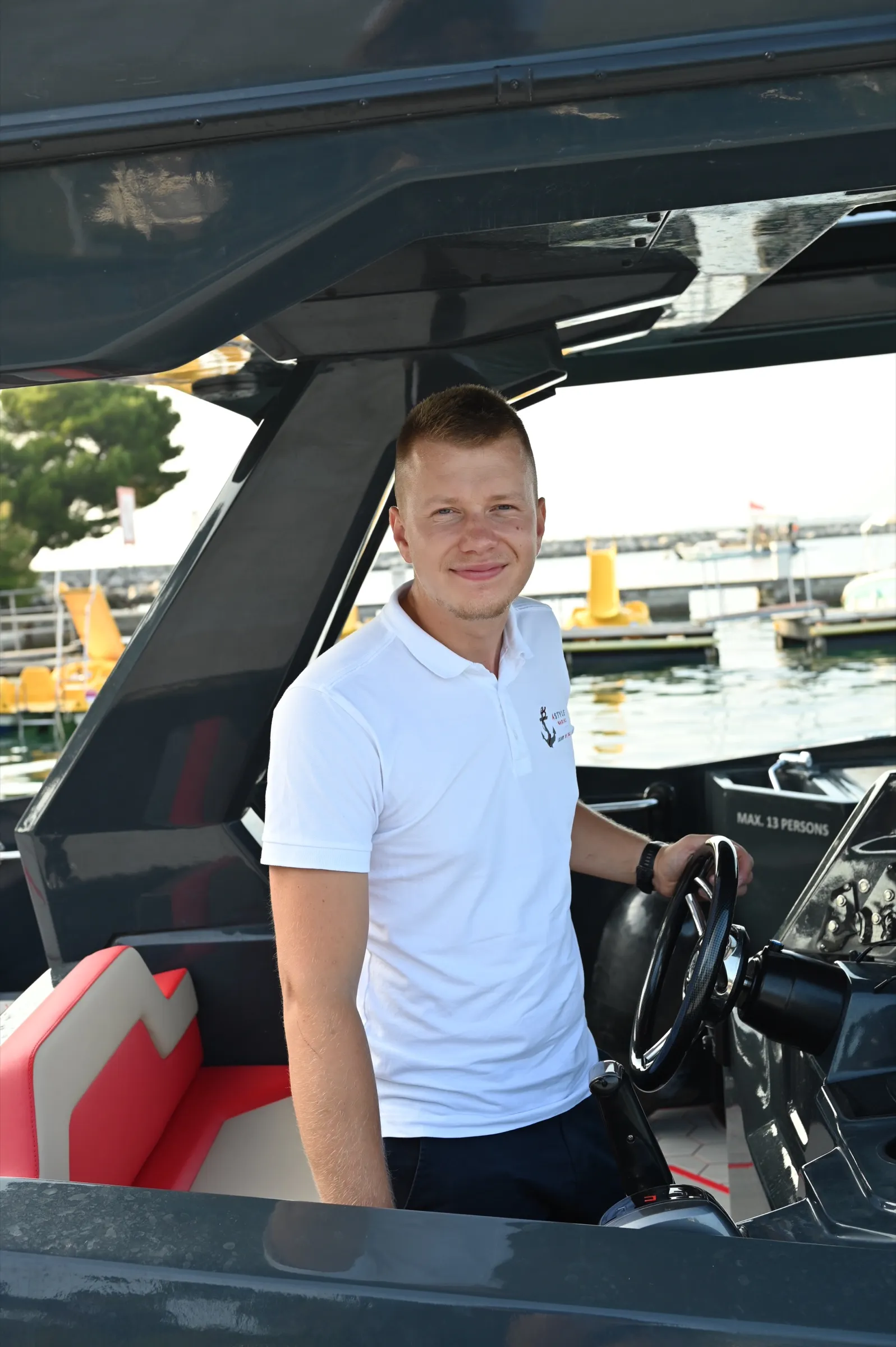 A crew member at the helm, the marina behind him