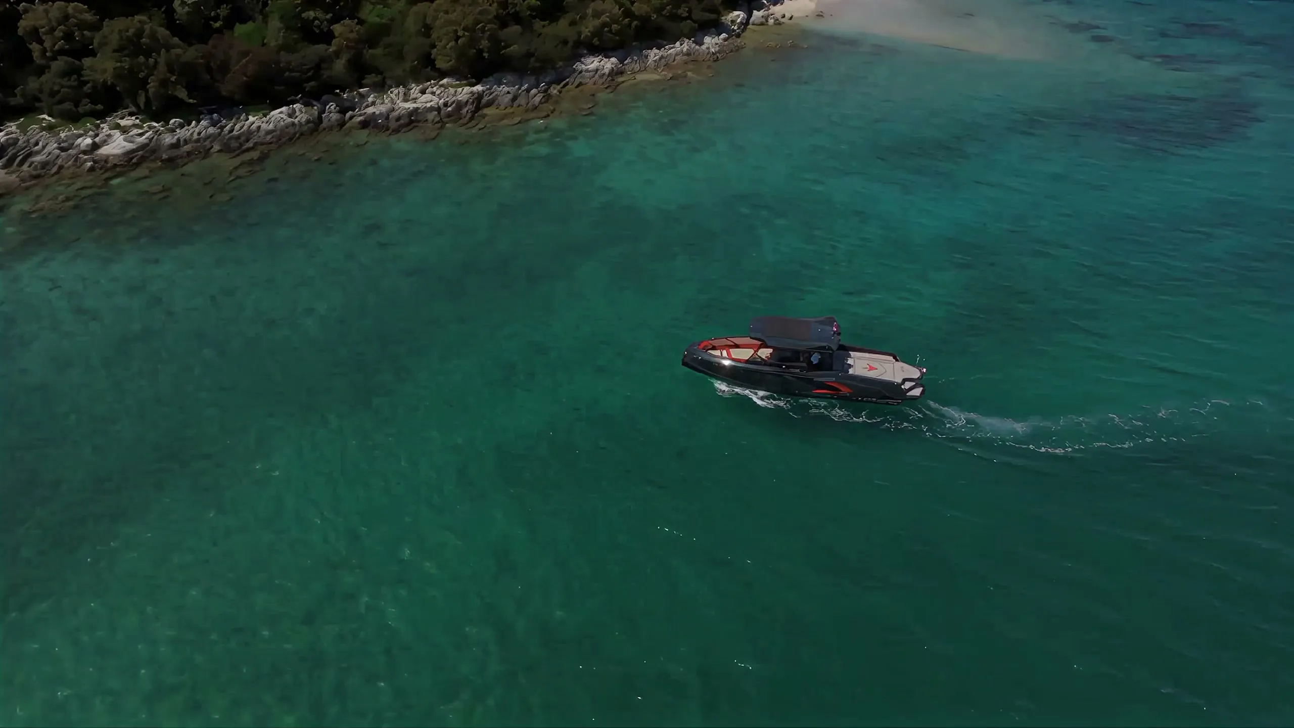 Het jacht van Astyle Marine vaart over turquoise water, dicht bij een rotsachtige kust